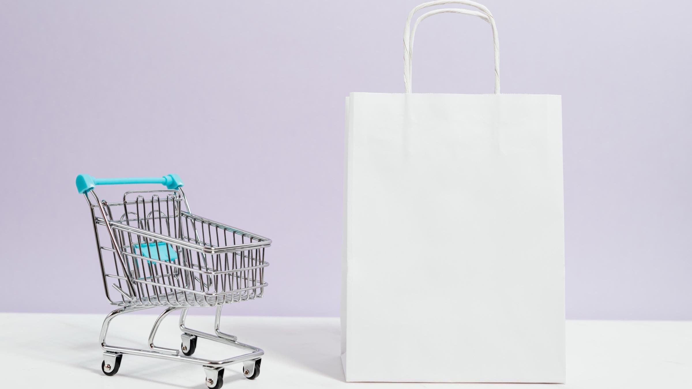 Carrito de compras miniatura y bolsa de tienda blanca sobre fondo lila — ecommerce retail B2C con IA en México